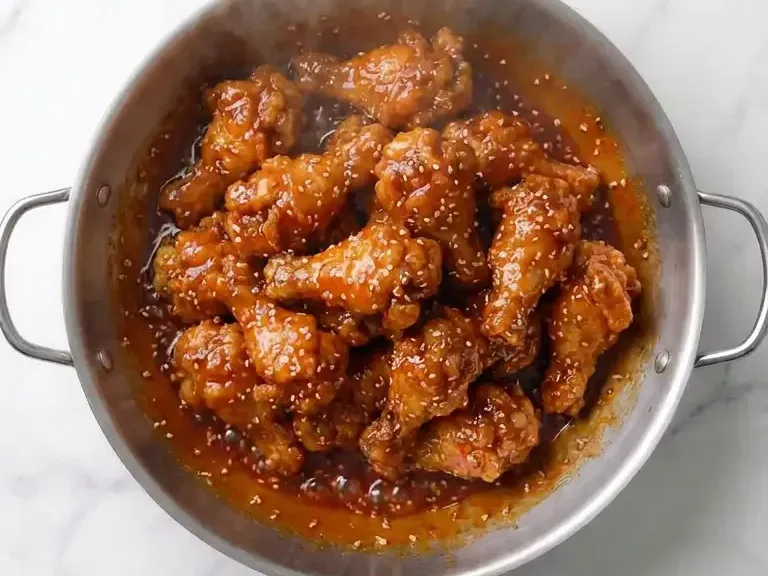 Fried chicken tossed in yangnyeom sauce in a wok