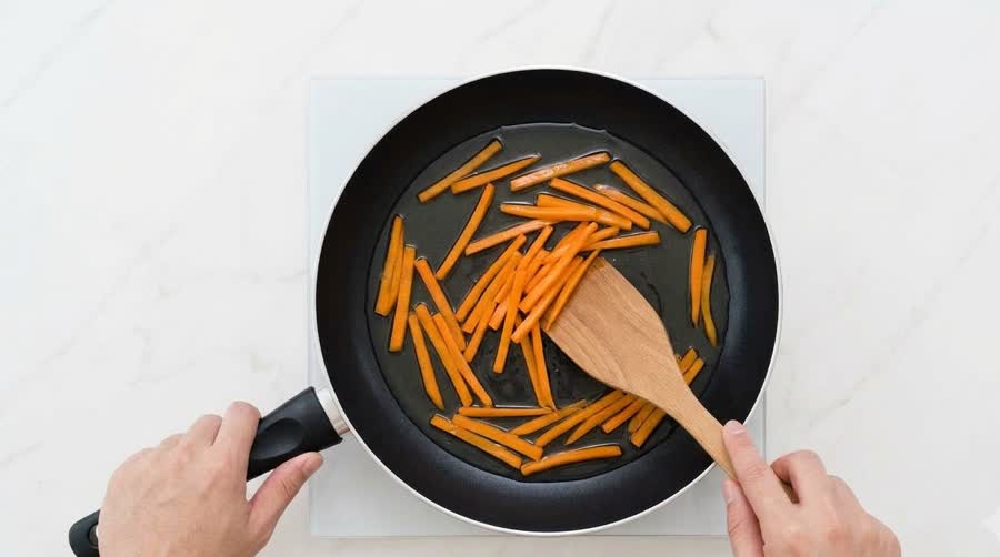 julienned carrots shallow-frying in a shallow pool of clear oil to make carrot oil for kimbap