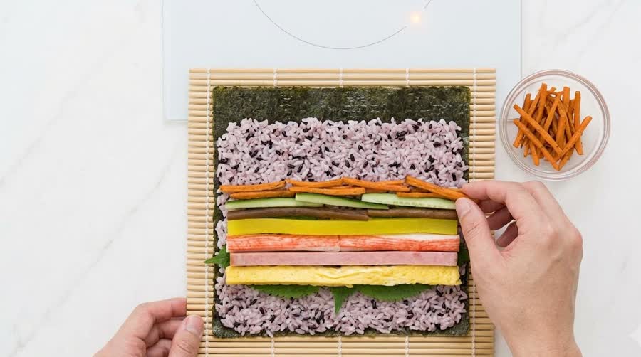 fried carrot and fillings lined up on a thin layer of rice on the seaweed for the kimbap recipe