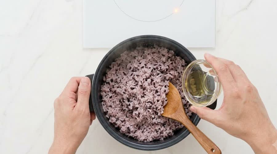 sesame oil poured into a pot of fresh black-rice mixed rice to season it for the kimbap recipe