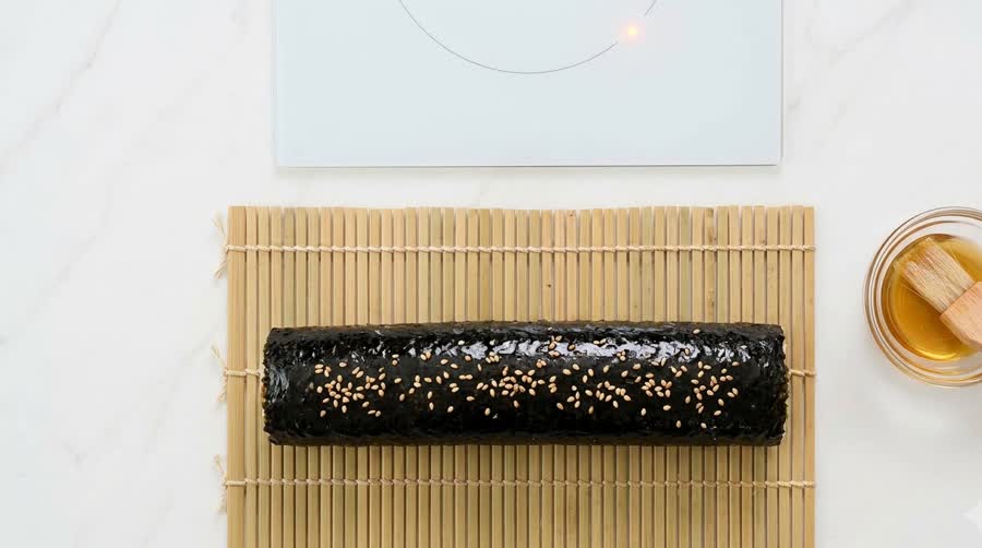 the finished kimbap roll brushed with sesame oil and sesame seeds on the bamboo mat