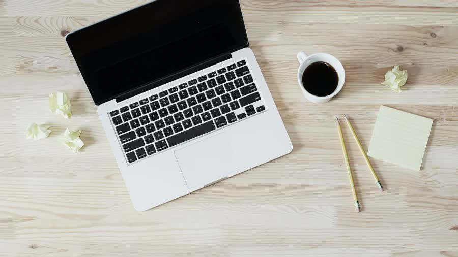 A flat lay of a minimalist remote work setup with a laptop, coffee and a notepad